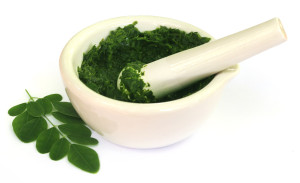 Moringa leaves with mortar and pestle over white background